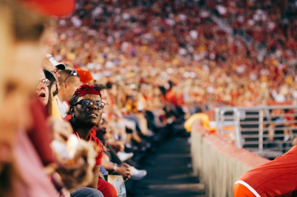 In a large sports crowd, a black woman with glasses watches intently.